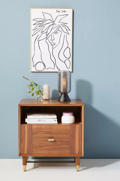 a wooden cabinet with two drawers and a painting on the wall above it, in front of a blue wall