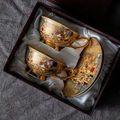 two golden cups and saucers sitting in a box on a gray cloth covered surface