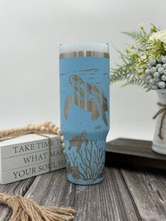 a blue tumbler sitting on top of a wooden table next to a vase with flowers