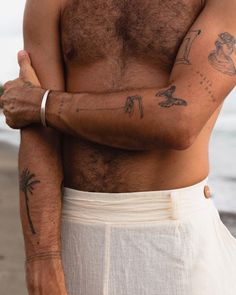 a shirtless man with tattoos on his arm and chest standing next to the ocean