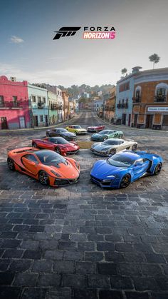 four different colored sports cars parked in the middle of an empty street with buildings on either side