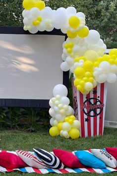 an outdoor movie party with balloons and popcorn buckets on the grass, in front of a large screen