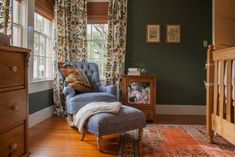 a blue chair sitting in front of a window next to a wooden dresser and baby crib