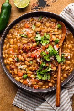 a bowl filled with beans and cilantro on top of a wooden table next to a spoon