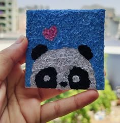 a hand holding up a small piece of felt with a panda bear on it's face