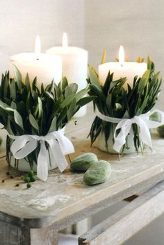 two white candles sitting on top of a wooden table next to flowers and leaves in vases