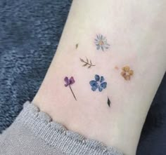 a woman's wrist with four different colored flowers on the left side of her arm