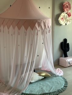 a pink canopy bed sitting on top of a wooden floor next to a white wall