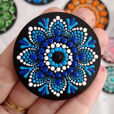 a hand holding a painted rock with blue and white dots on it's surface