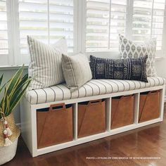 a white bench with storage bins and pillows on it in front of a window