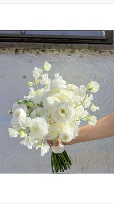 a bouquet of white flowers being held by someone's hand in front of a building