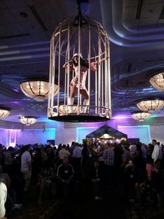 a man standing on top of a cage in the middle of a room filled with people