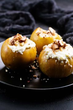 three baked apples with cream and nuts on a black plate