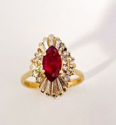 a ring with a red stone surrounded by white and yellow diamonds on a white surface