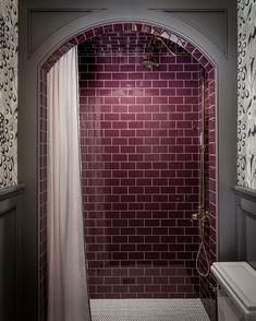 a bathroom with a red brick wall and white toilet next to a shower stall in the corner