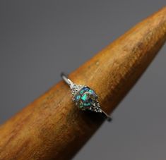 an opal and diamond ring sitting on top of a wooden stick