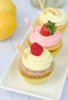 three cupcakes with white frosting, raspberries and strawberries on top