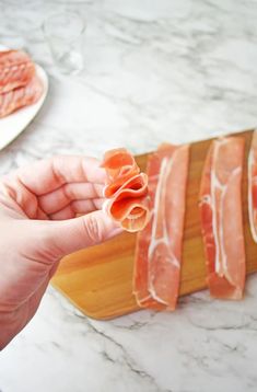 a person is holding some meat on a cutting board with other food items in the background