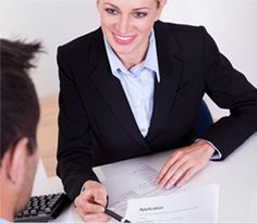 a woman sitting at a desk with a man in front of her holding a piece of paper