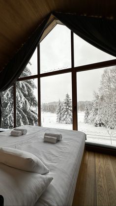 a bed with white sheets and pillows in front of a large window that overlooks snowy trees