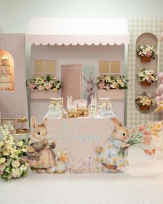 a table topped with lots of stuffed animals next to a pink doll house and flowers