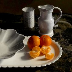 two oranges are sitting on a plate next to a pitcher and glass vase,