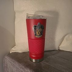 a red tumbler cup sitting on top of a table next to a white pillow