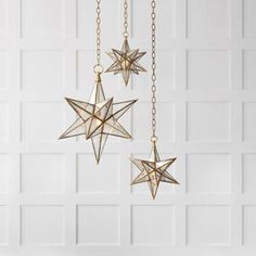 three gold stars hanging from chains against a white wall