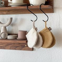 some pots and pans are hanging from hooks on the wall in front of cups