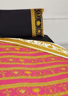 a pink and gold bed spread with black pillow cases on top of it, in front of a white wall