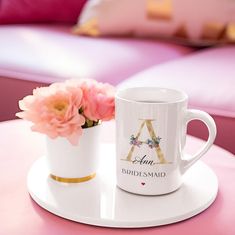 two coffee mugs sitting on top of a pink table next to each other with flowers in them