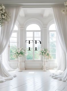 a room with white curtains and flowers in vases on the floor next to windows