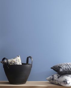 a black basket sitting on top of a wooden table next to pillows and a pillow