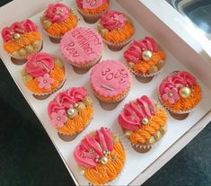 cupcakes decorated with pink, orange and gold icing in a white box