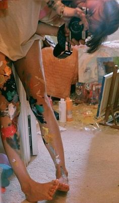 a woman with her legs covered in paint and holding a camera next to the floor