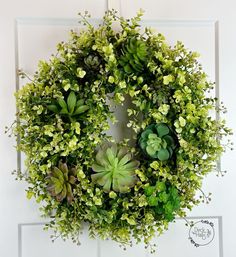 a wreath with succulents and greenery hanging on a door