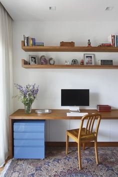 a desk with a computer on top of it next to a blue drawer and chair