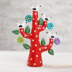 a red tree with birds and flowers painted on the branches is sitting on a table