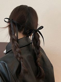 a woman wearing a black leather jacket with two braids in her hair, looking off to the side