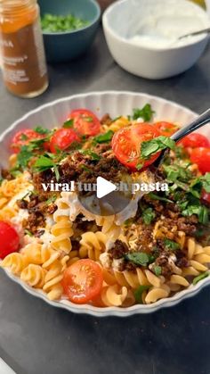 a bowl filled with pasta and vegetables on top of a table next to bowls of dressing