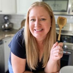 a woman sitting at a kitchen table with a wooden spoon in front of her face