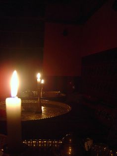 two lit candles sitting on top of a table in a dark room with other items