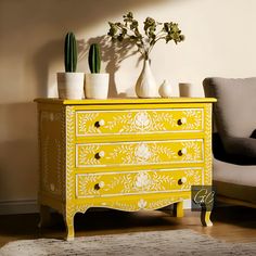 a yellow chest of drawers sitting in a living room next to a chair and potted plants