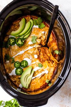 a crock pot filled with chicken enchiladas and topped with avocado