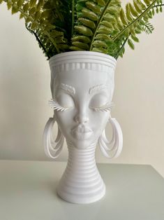 a white vase with a plant in it and a face on the side, sitting on a table