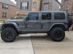 a gray jeep is parked in front of a house on the sidewalk with black tires