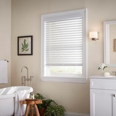 a bathroom with a tub, sink and window covered in white blind shades on the windowsill