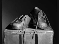 black and white photograph of two pairs of shoes on top of an old suitcase with straps