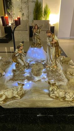 three statues of angels sitting on top of a table with lights in the middle and candles lit up behind them