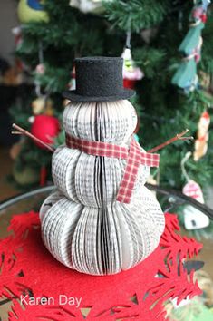 a snowman made out of yarn sitting on top of a table next to a christmas tree